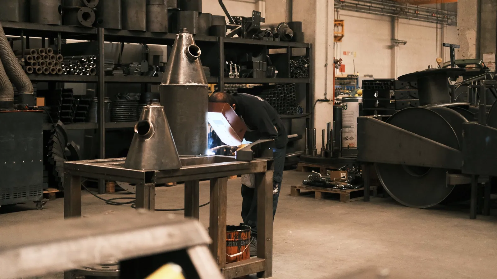 Welder working on a fabricated metal component in an industrial workshop.